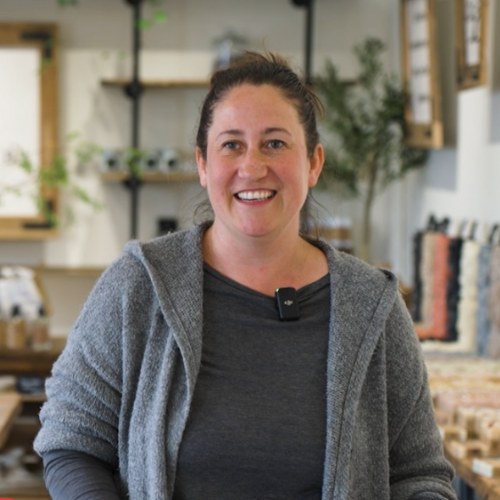 A white woman smiling with brown hair tied back and a grey shirt