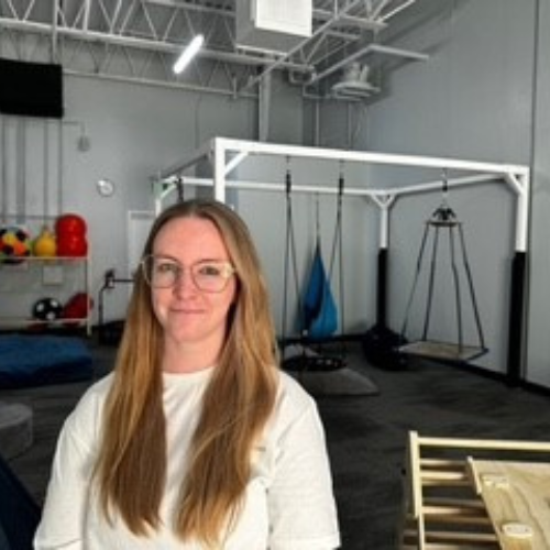 A white woman with long straight blonde hair wearing a white sweater in a gym facility