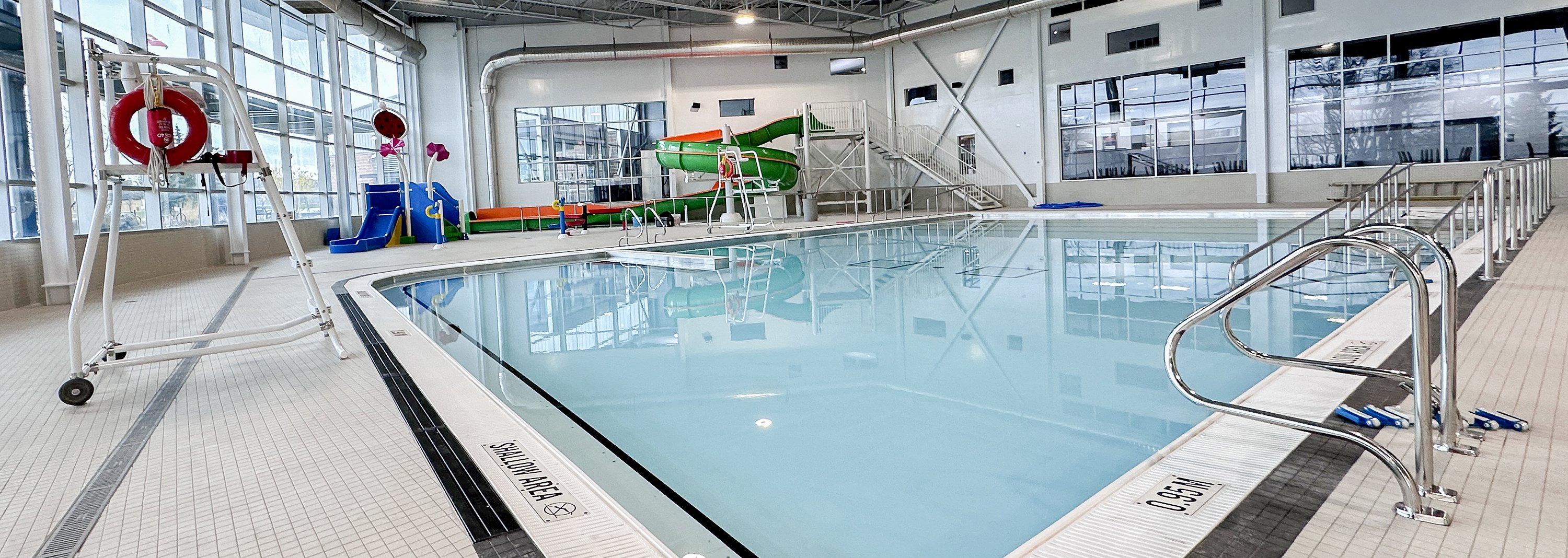 A pool with a lifeguard chair to the left and an indoor play area and water slides behind it