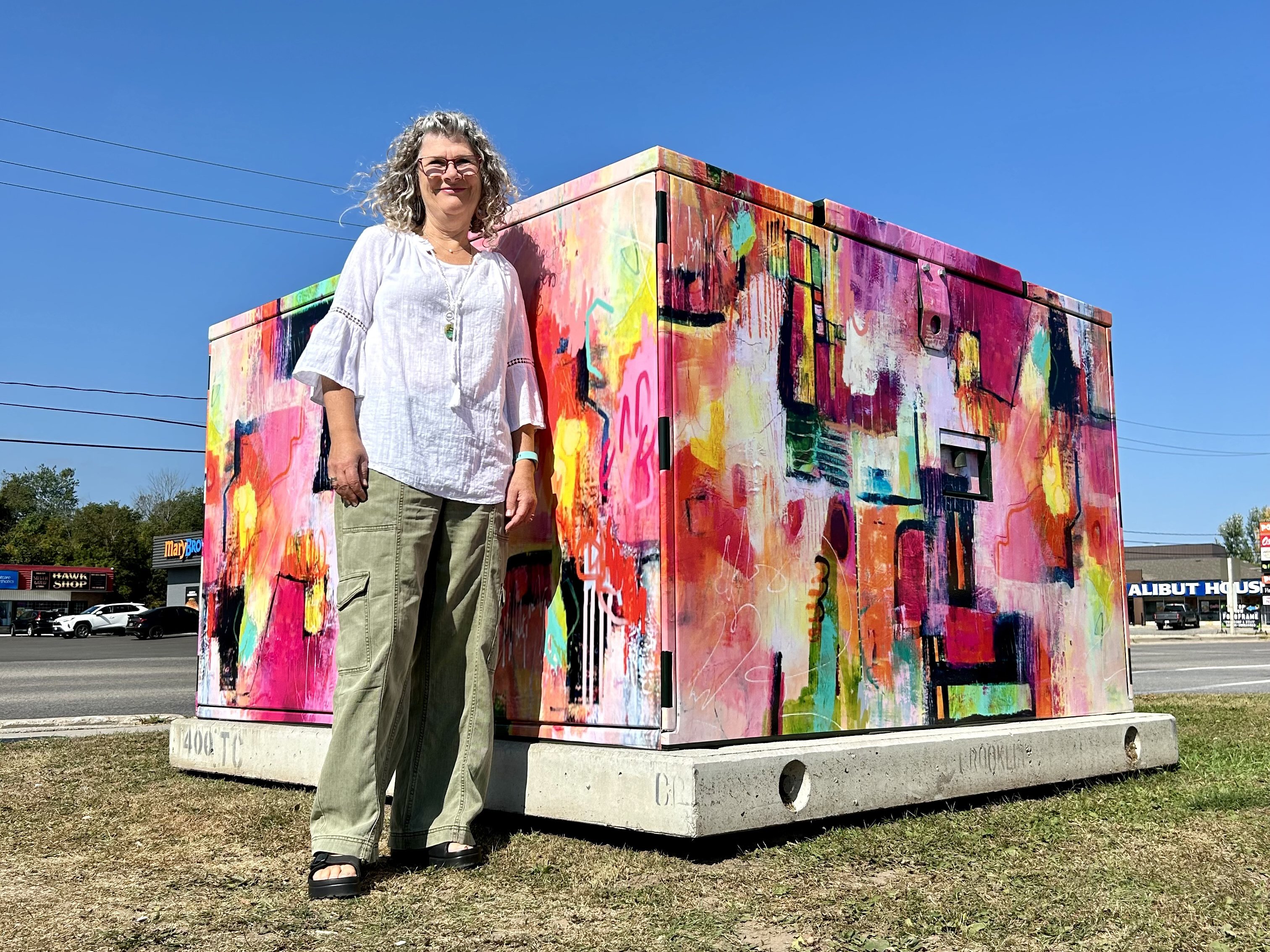 An artist stands next to a utility box covered in brightly coloured artwork