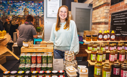 Woman at an indoor farmers' market, selling honey products